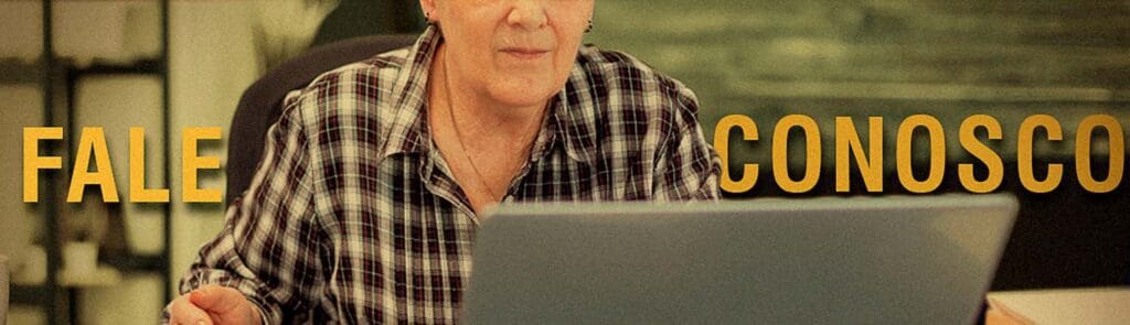Foto de uma idosa sentada em uma cadeora olhando o computador com o texto "Fale Conosco" atrás.